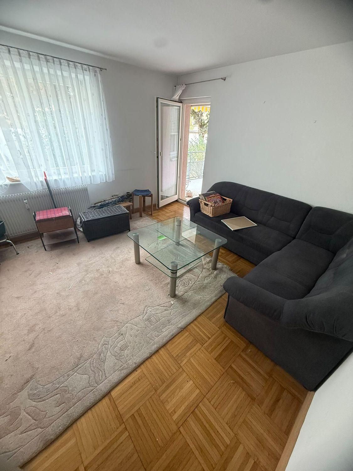 Wohnzimmer vor der Entrümpelung mit Eckcouch, Glastisch und Teppich