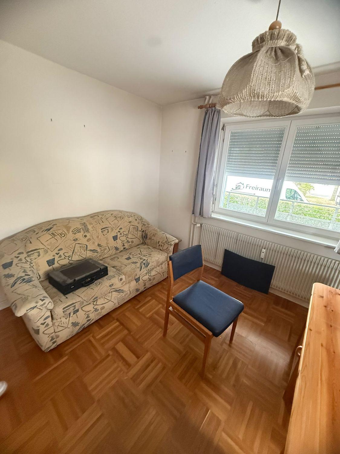 Zimmer mit altem Schlafsofa und Stühlen, draußen das Fahrzeug von Freiraum Dienstleistungen