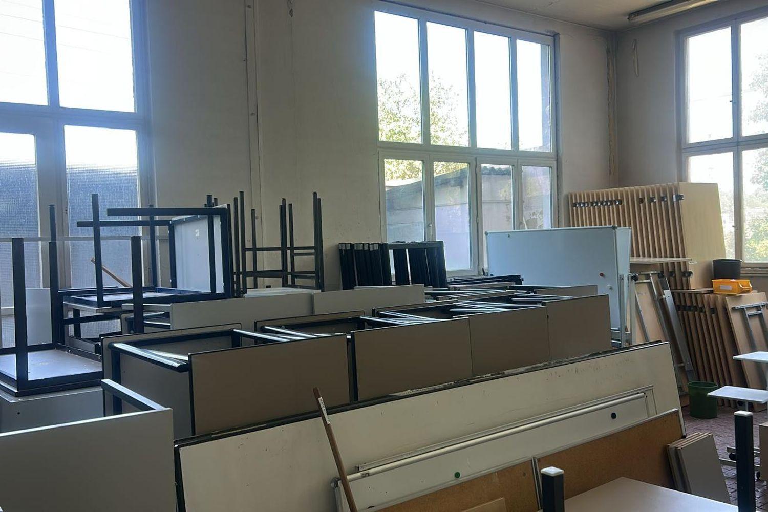 Vollgestellter Raum mit gestapelten Tischen, Stühlen, Tafeln und Garderoben vor der Räumung